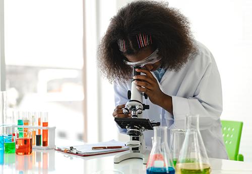 Female looking through microscope in lab.